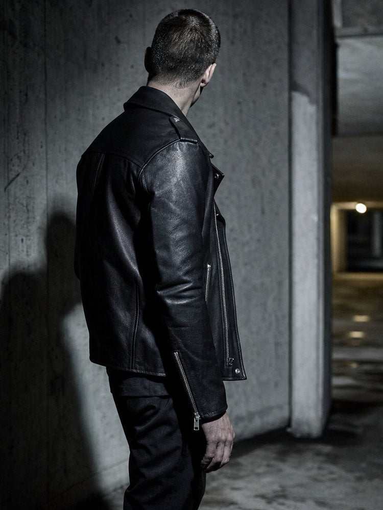 Man in a black ROCQERX faux leather biker jacket in a concrete underpass