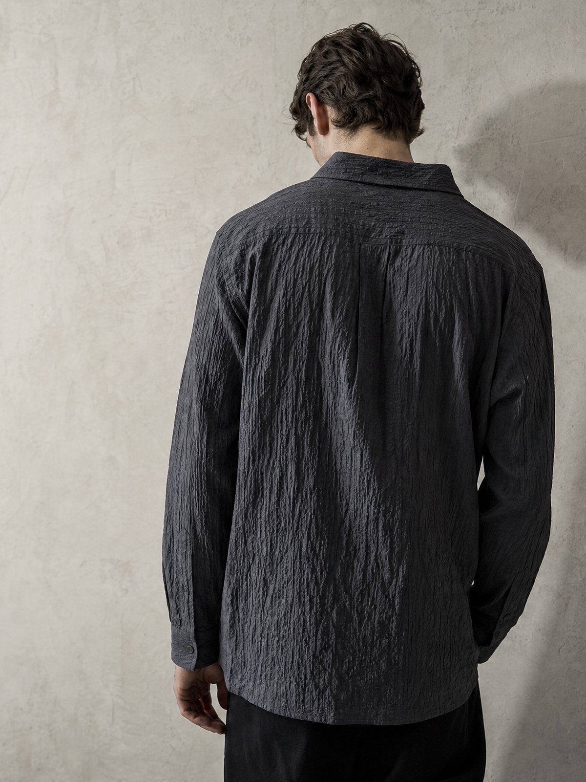 Man in a ROCQERX textured long-sleeve shirt against a pale plaster wall